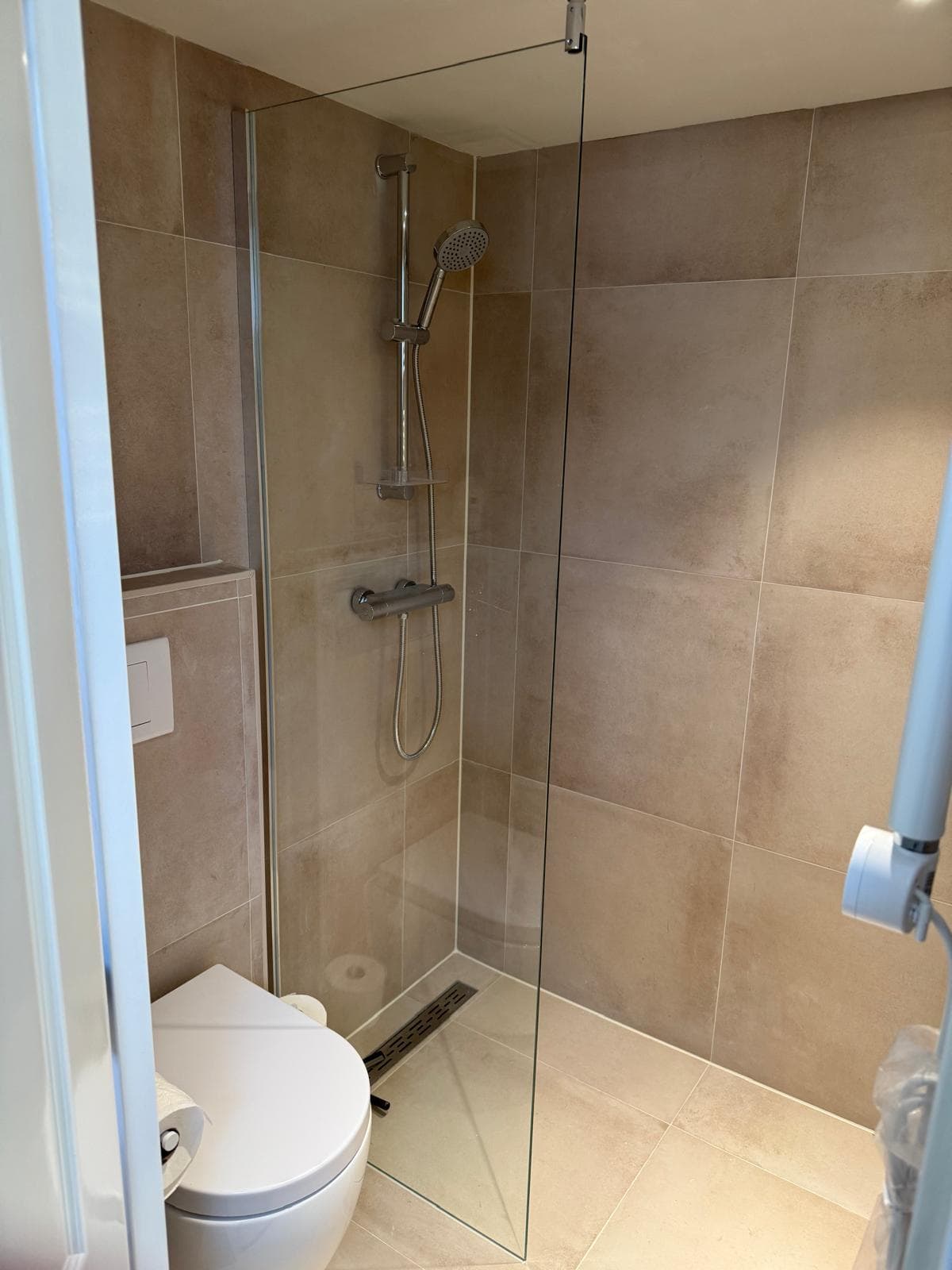 Inloopdouche en hangtoilet in een badkamer met beige tegels