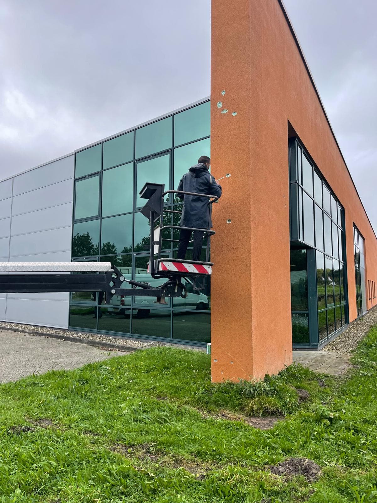 Vakman op een hoogwerker werkt aan de gevel van een bedrijfspand