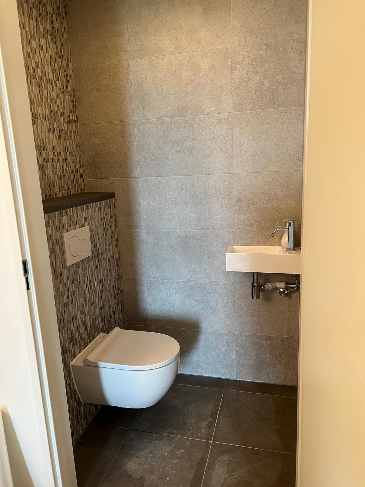 Toilet met mozaïektegels op de voorzetwand